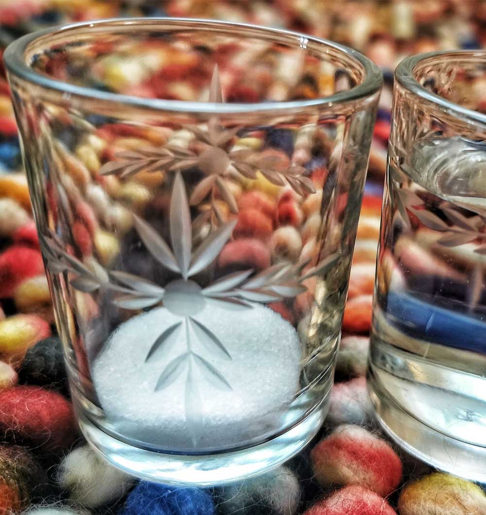 Zwei Gläser mit spirituellen Zeichen. Das Glas links ist leer. Das Glas rechts ist mit Wasser gefüllt.