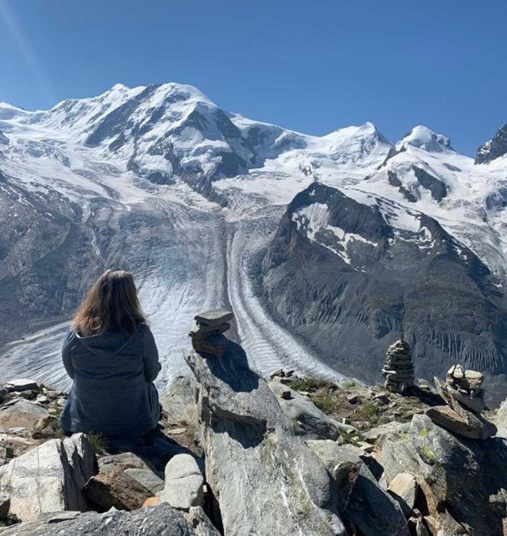 Frau sitzt auf einem Stein vor Bergpanorama