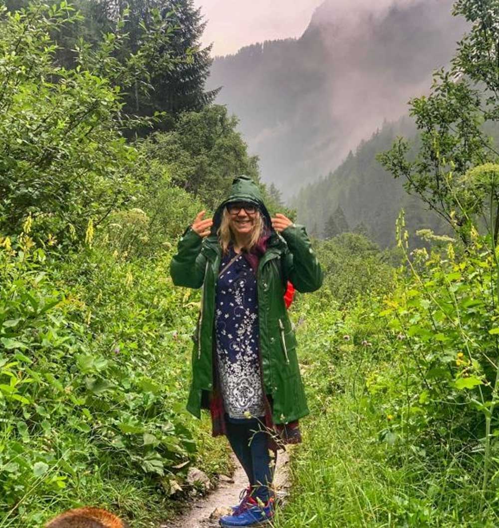 Manuela Krah steht in einem Regenmantel auf einem Wanderweg mitten in einem grünen Wald.